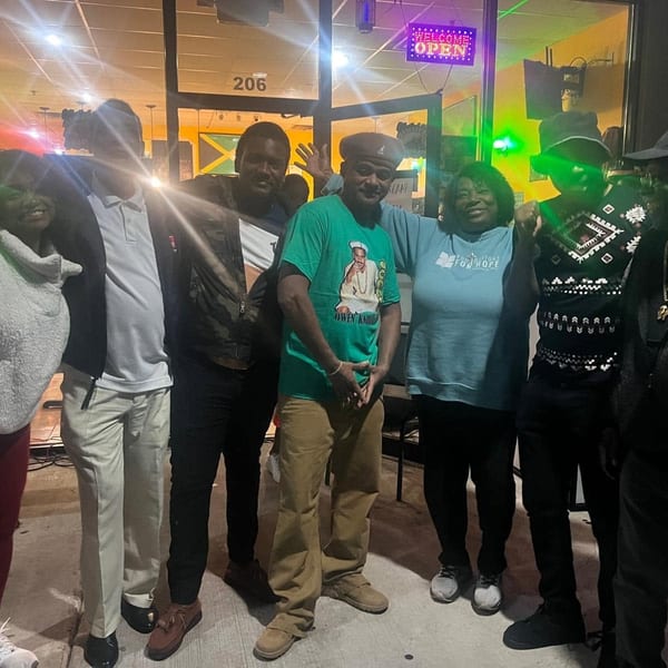 Seven people smiling and posing together outside a restaurant at night with an "OPEN" sign.