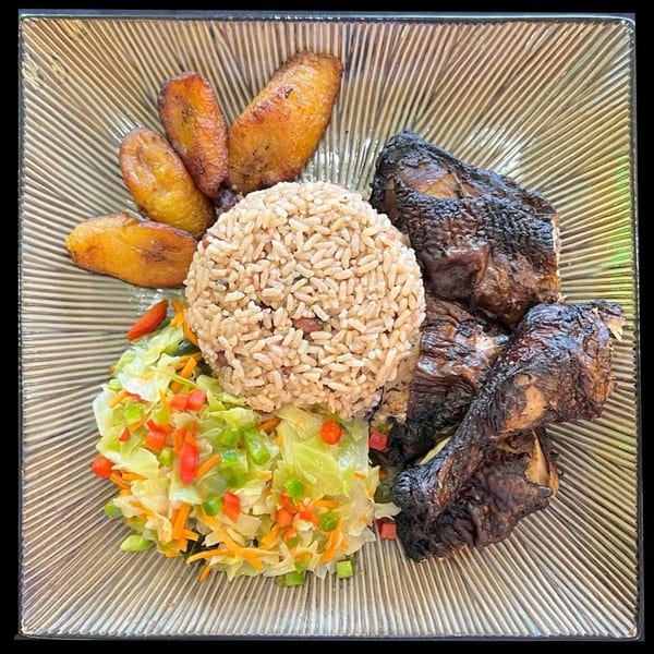 A plate of jerk chicken, rice and peas, fried plantains, and steamed cabbage with bell peppers.