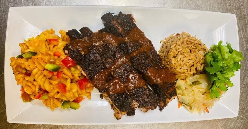 Grilled ribs with sauce, pasta salad, rice, and cabbage on a white rectangular plate.
